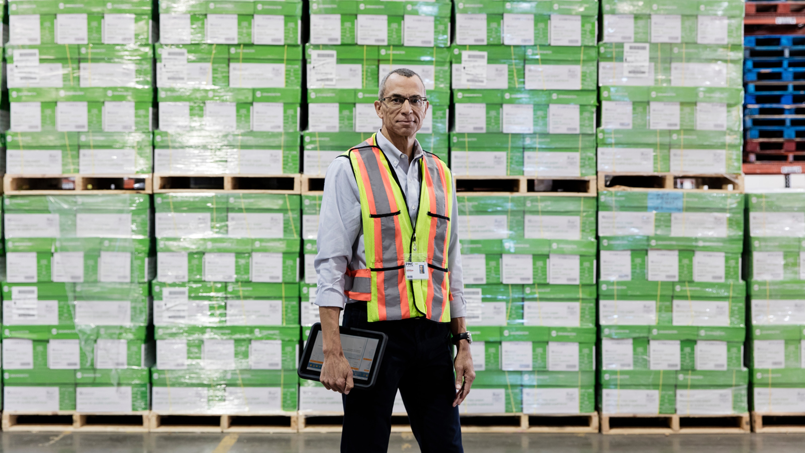 Portrait of worker holding digital tablet and standing near pallets in industrial shipping warehouse.