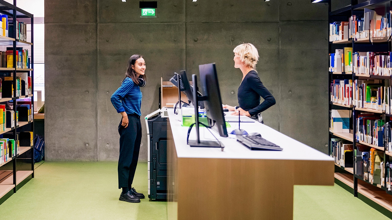 A student talking to a librarian, asking for help in a large, modern library.