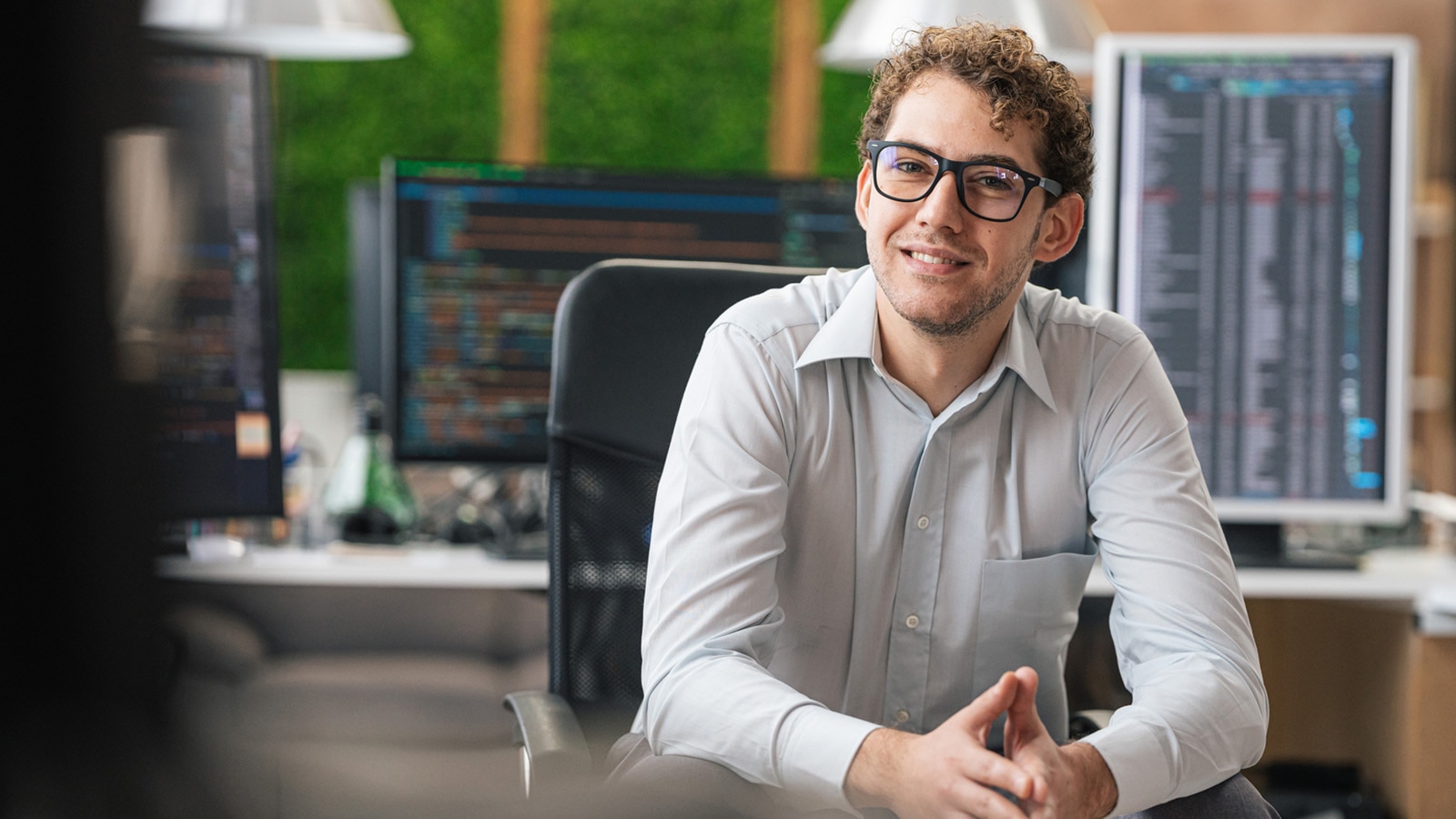 Portrait d’un programmateur informatique souriant assis à côté d’ordinateurs de bureau.